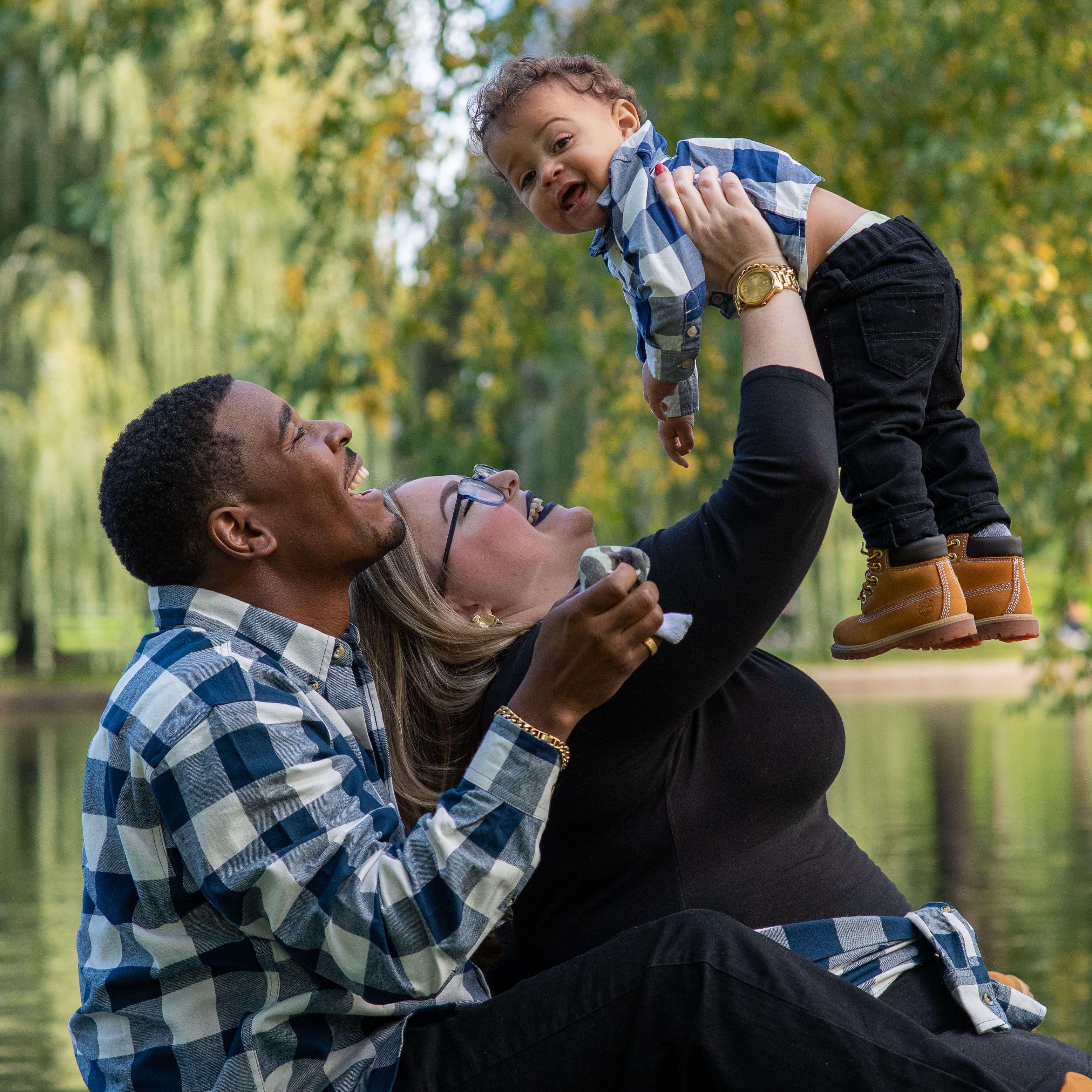 A joyful couple lifting a laughing toddler in the air at a park.