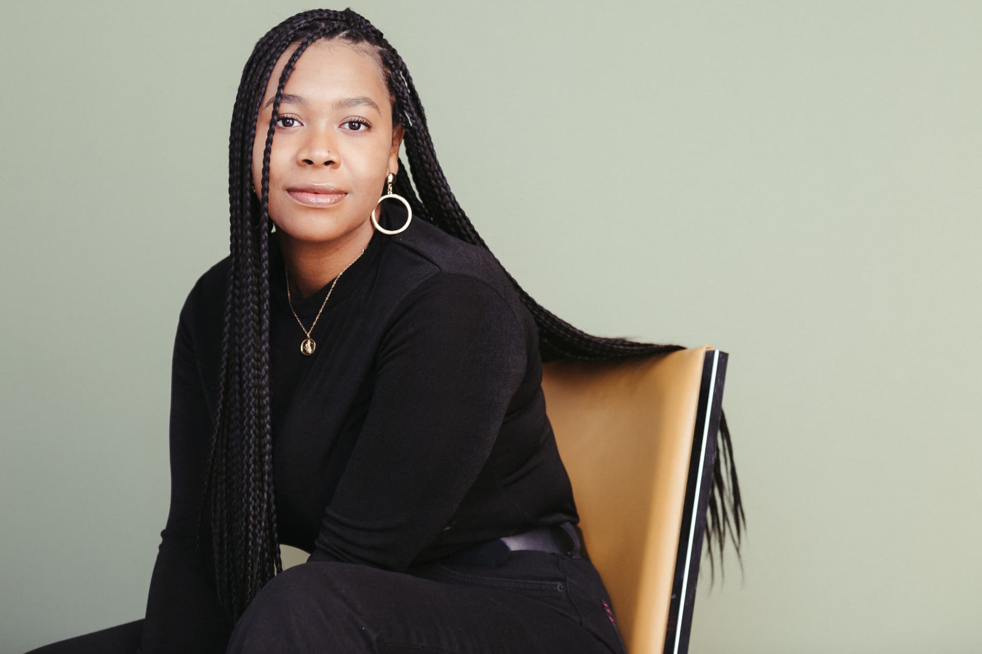 A woman with braided hair sitting in a chair against a green background.