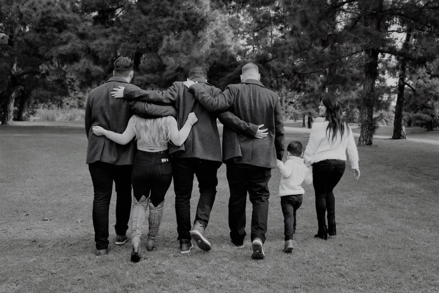 A black and white photo of a group walking away with arms around each other in a park setting