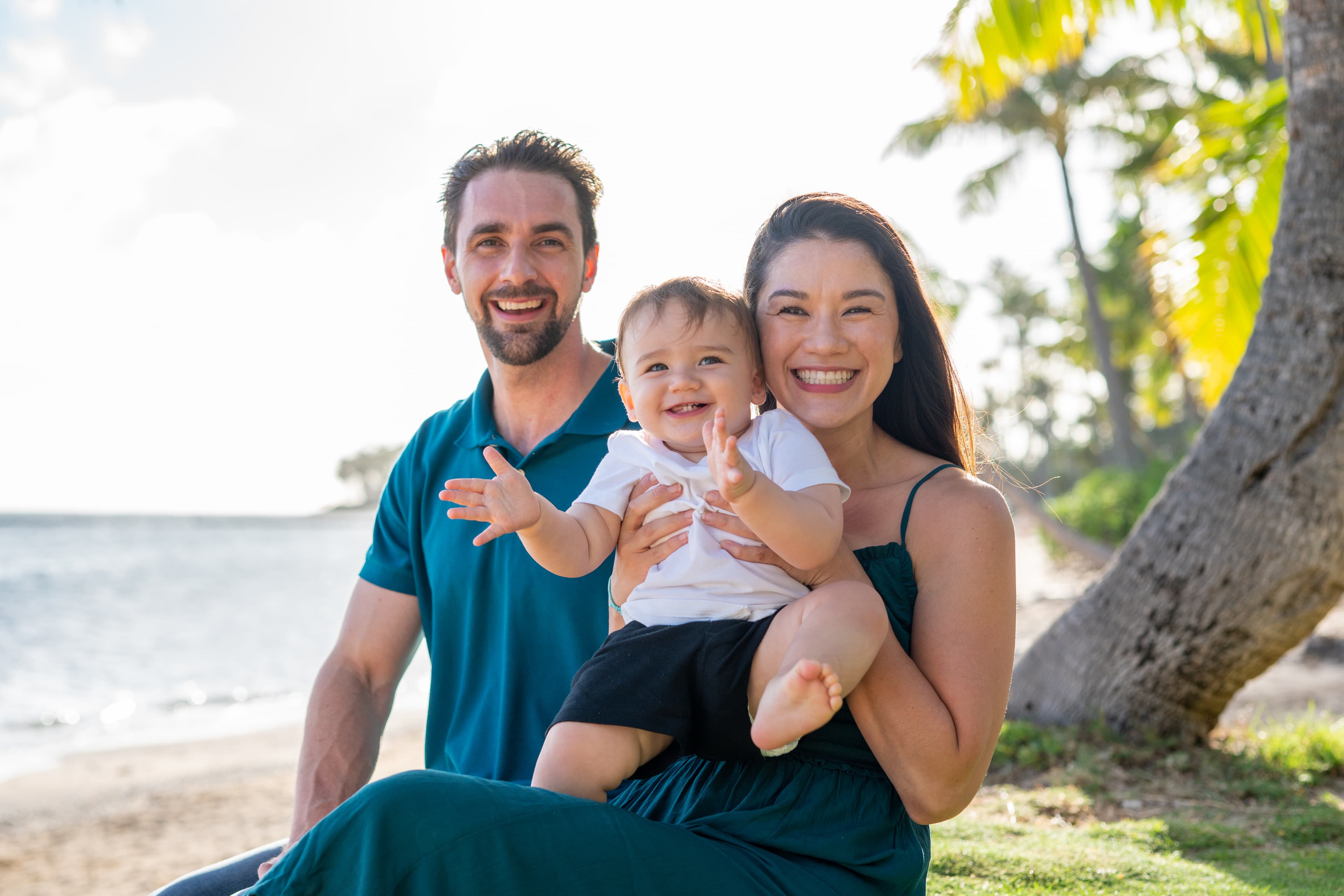 Happy family with a toddler smiling on a tropical beach with palm trees.