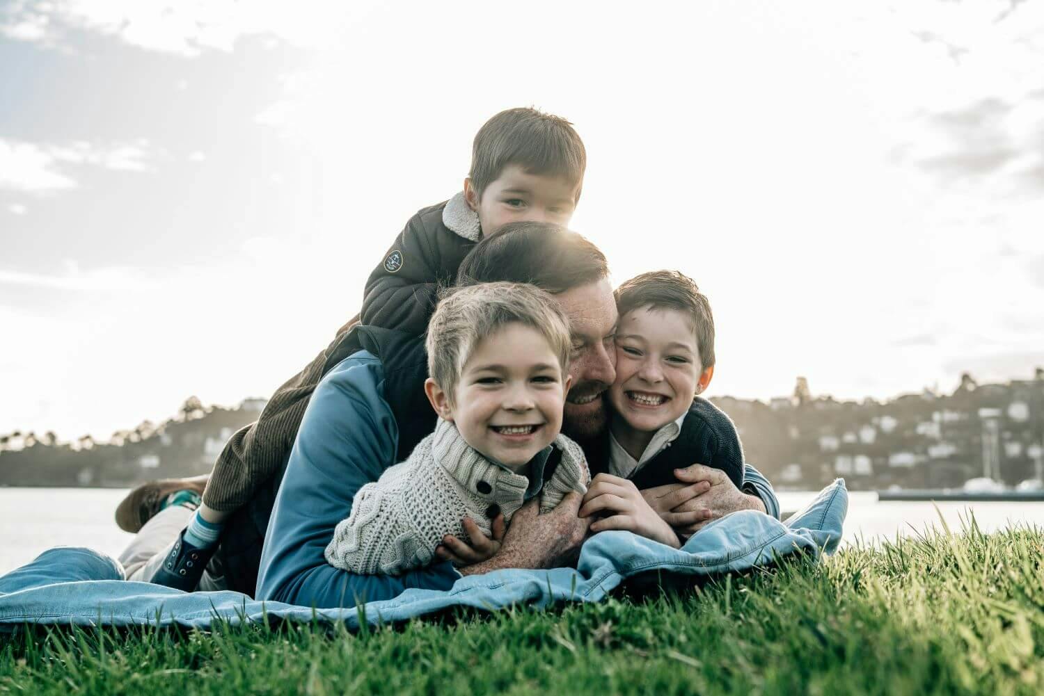 Three children piled on top of an adult, lying on grass in a park