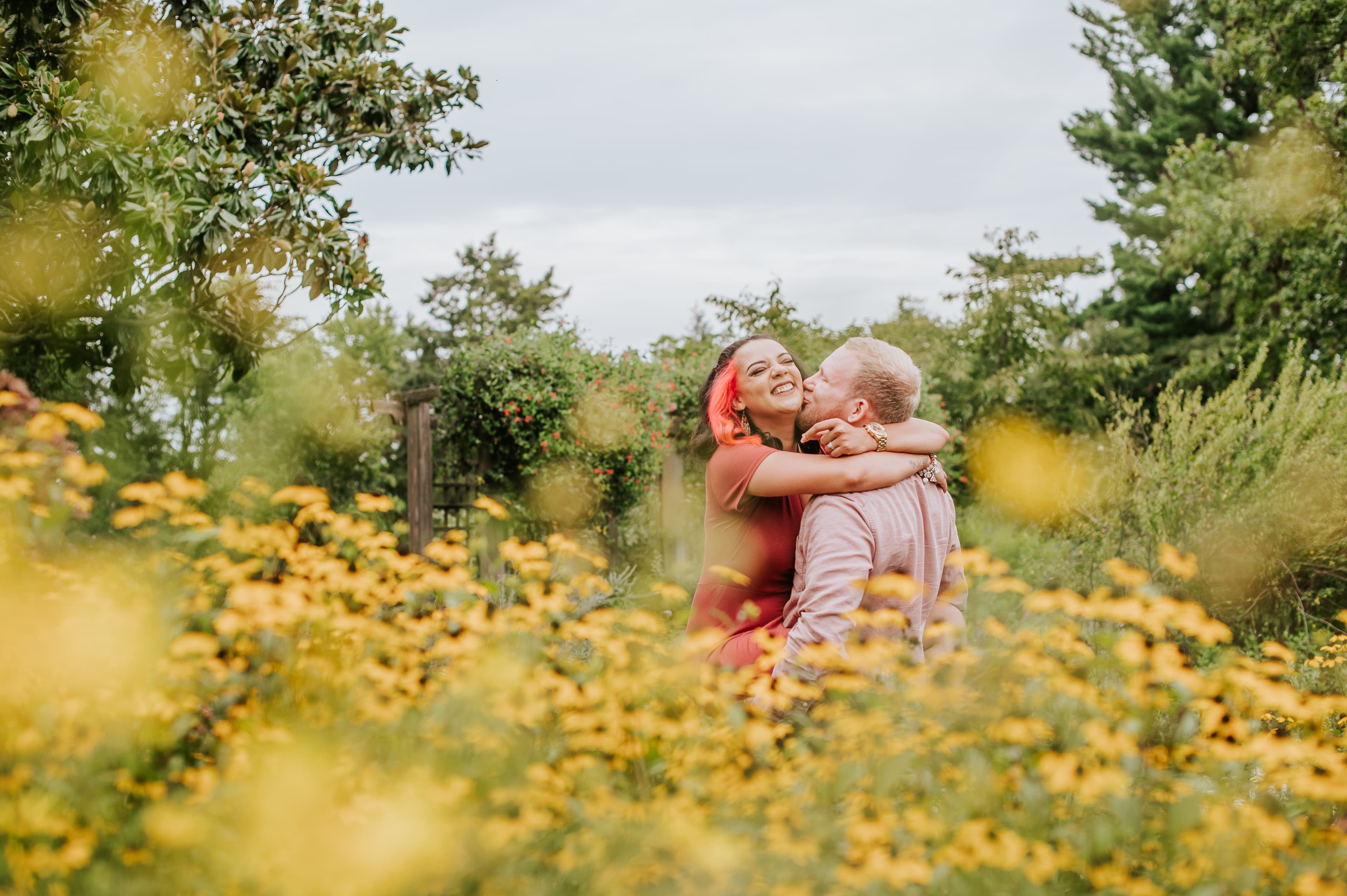 Couple embracing and laughing in a garden full of yellow flowers.