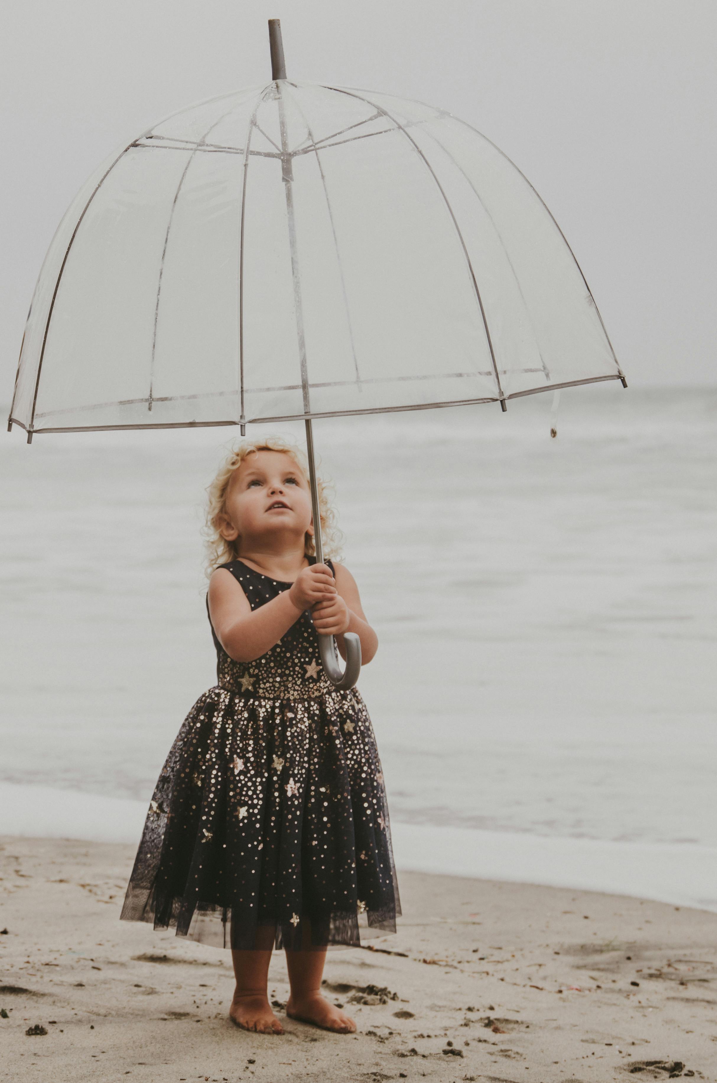 photo of a young girl on a beach under a transparent umbrella