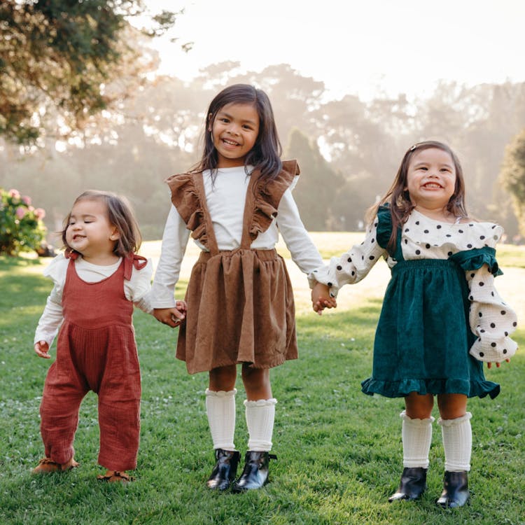 Three young girls holding hands and smiling in a park