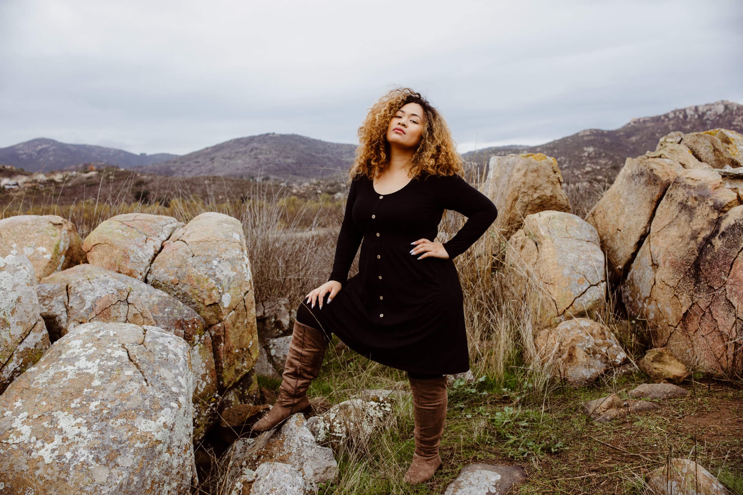 A confident woman posing in front of rocks and a natural landscape