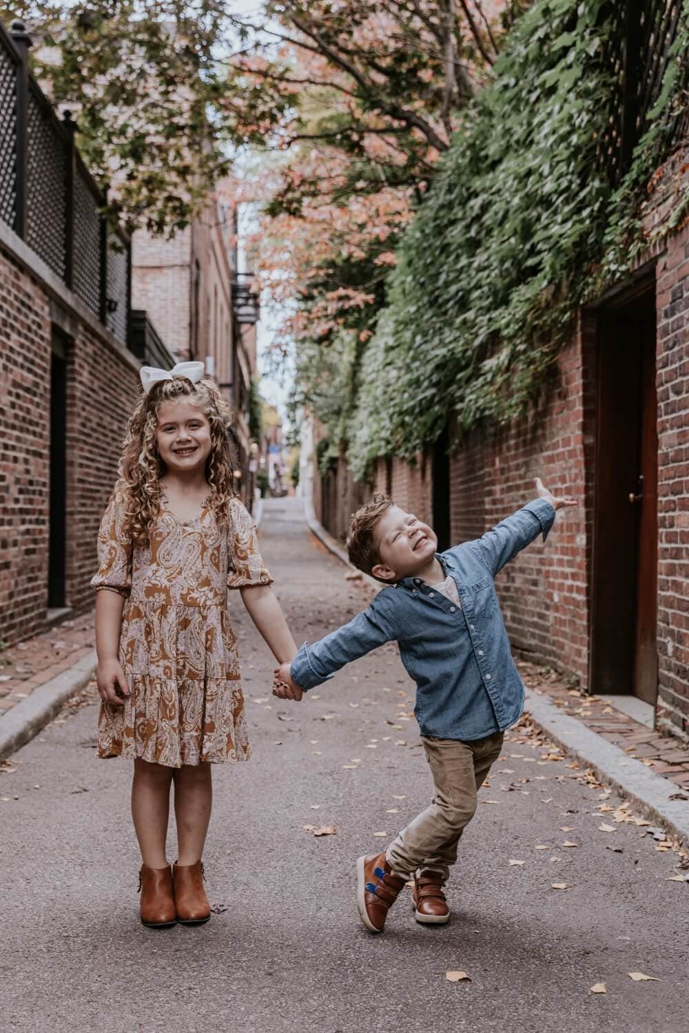 Two children walking hand in hand down a brick-lined street.