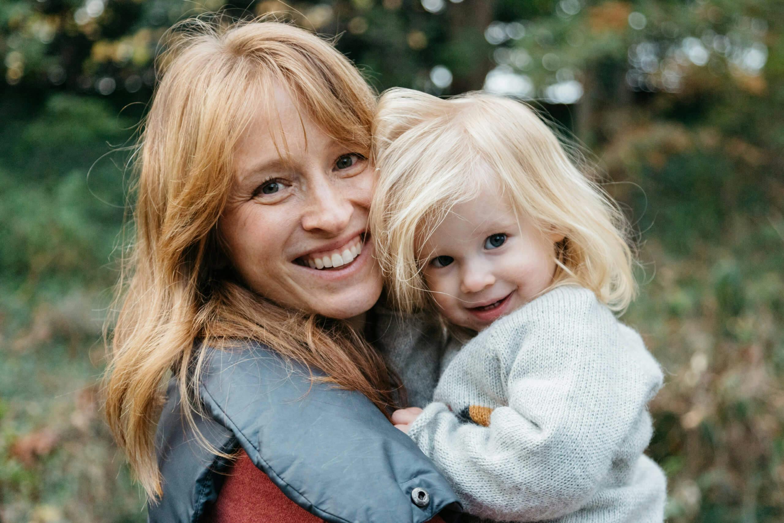 Smiling woman holding a young blonde child in a nature setting