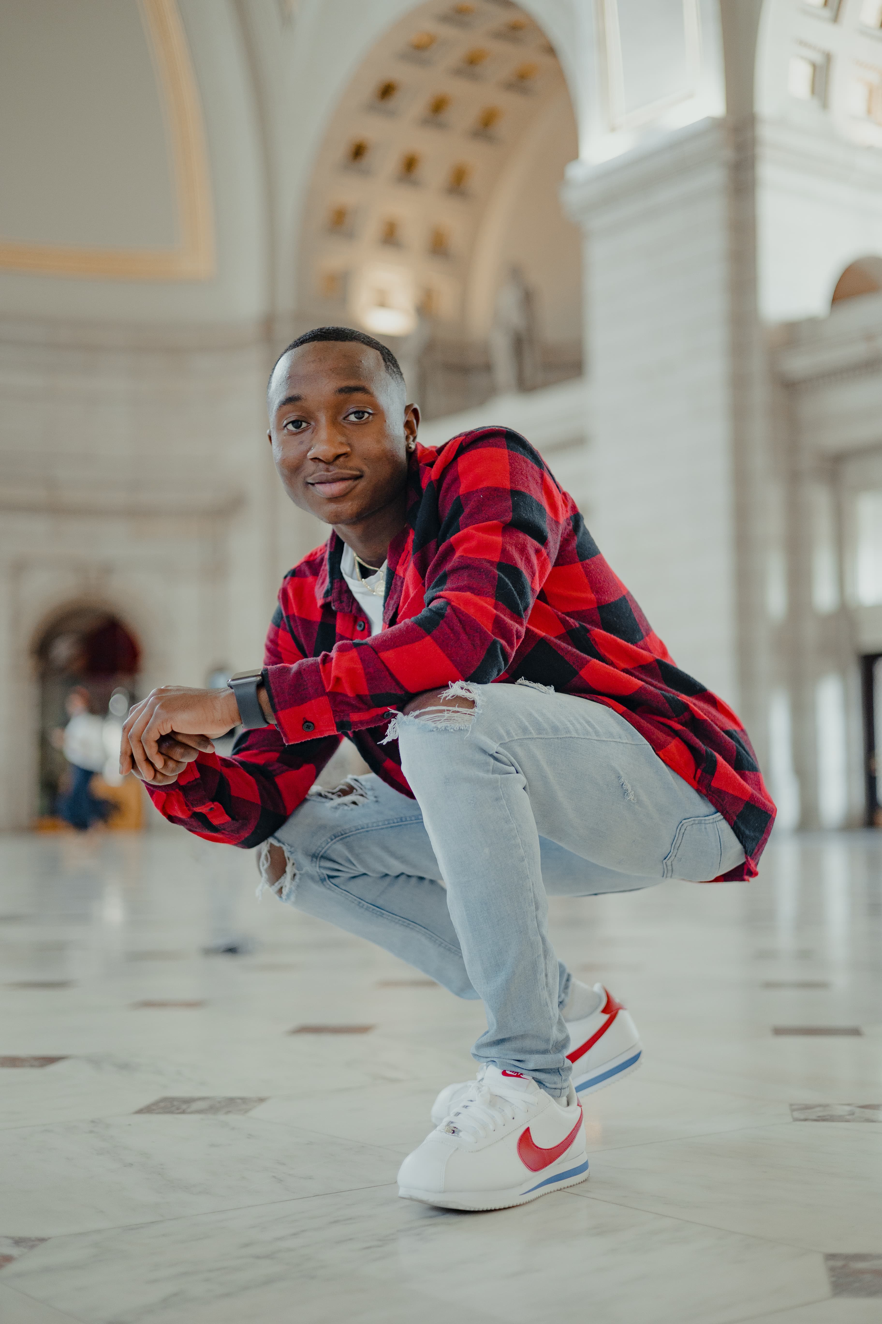 Young man in a red plaid shirt crouching in an elegant interior with arches.