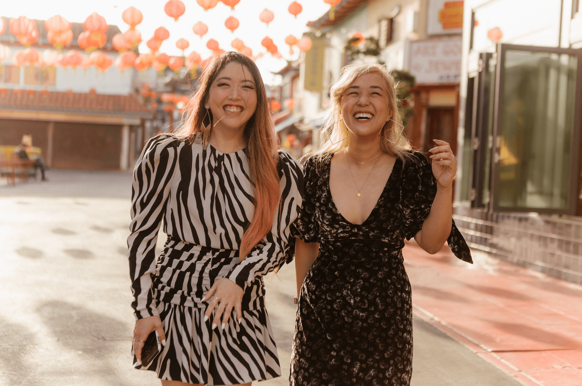 Two happy women walking and laughing together on a street decorated with lanterns.