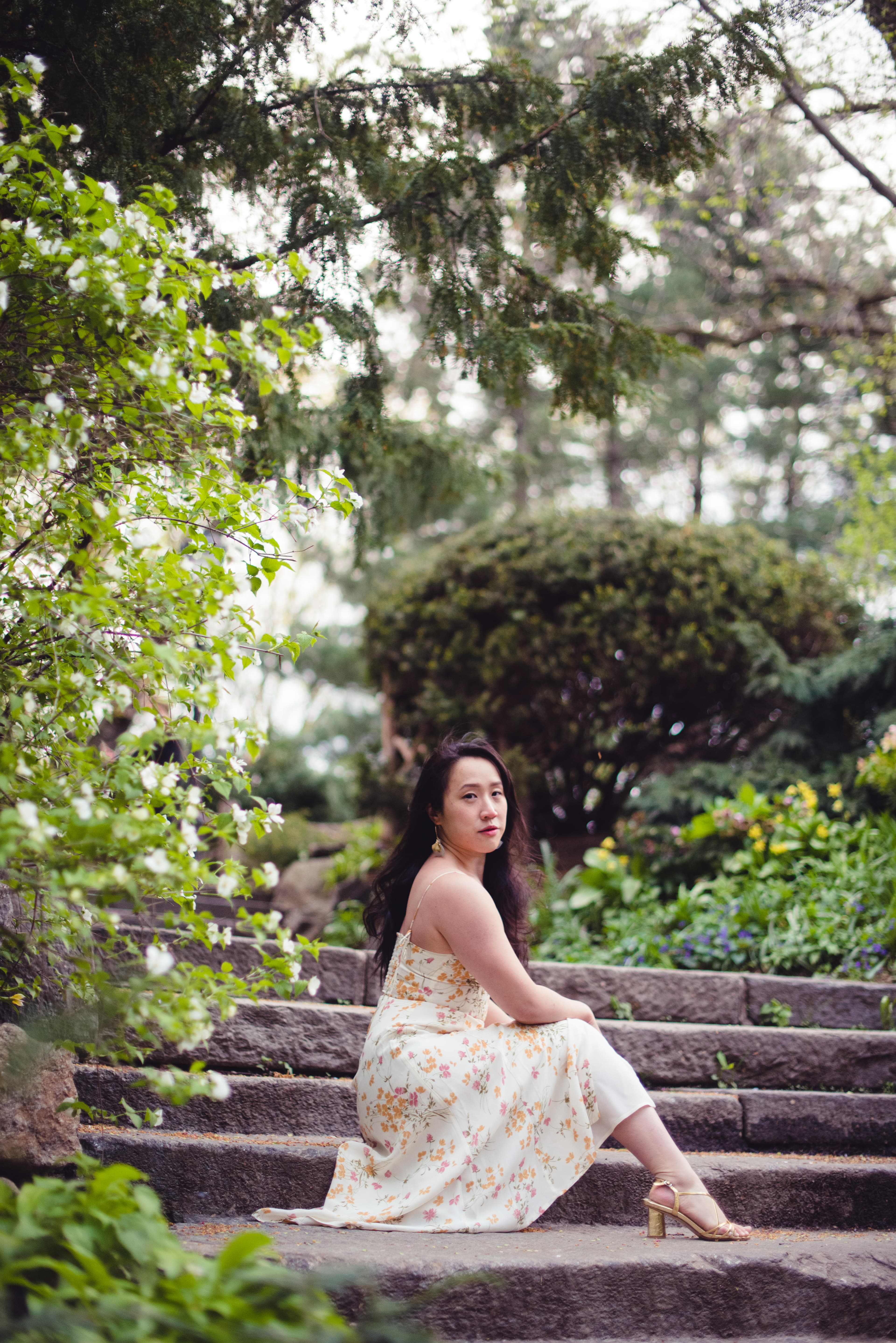 Woman sitting thoughtfully on stone steps in a garden with blossoming trees.